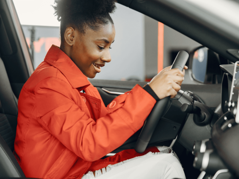 A happy African woman sitting in the driving seat of a car, preparing to drive away.