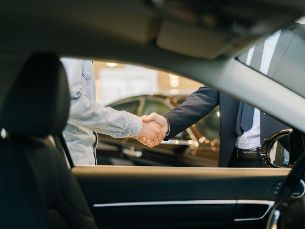 Buyer and seller shaking hands over a vehicle sale representing confidence and strong car resale value.
