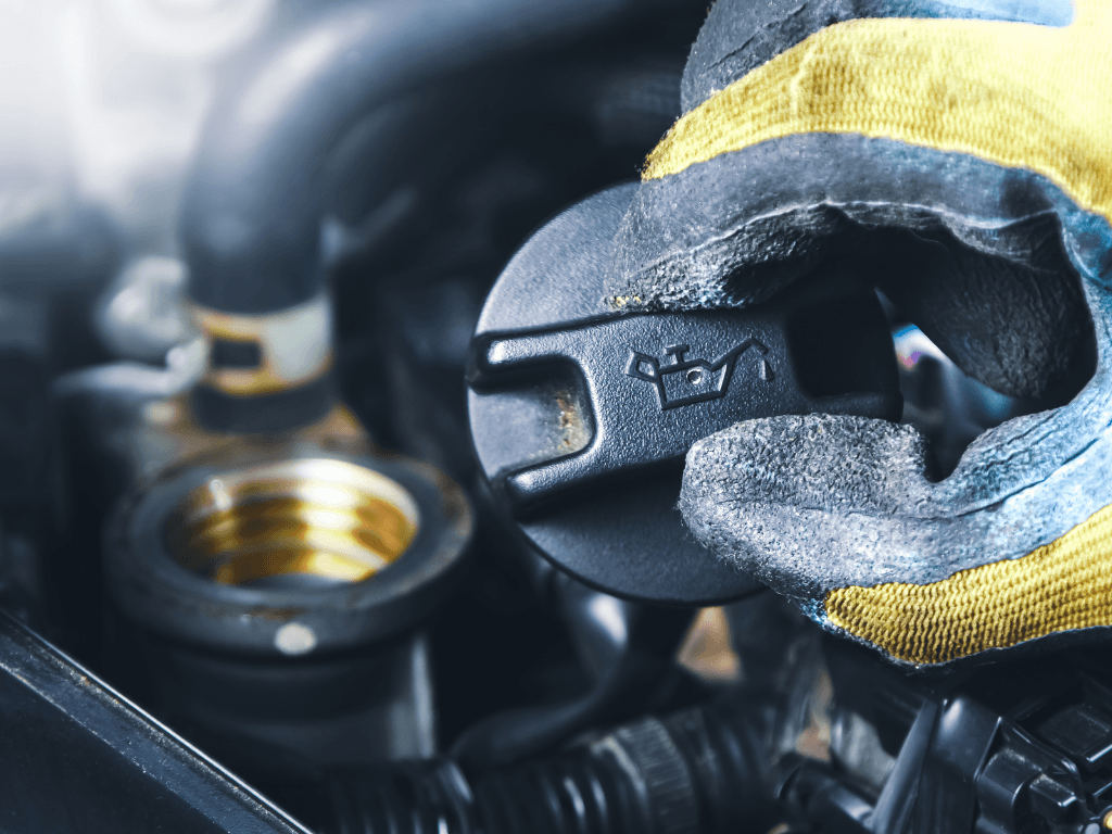 Removing an engine oil filler cap to check for sludgy residue when buying a used car.